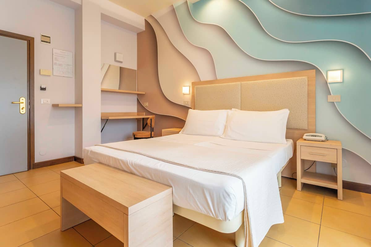 A modern hotel room with a large bed, bedside tables, a bench, and a unique wavy wall design.