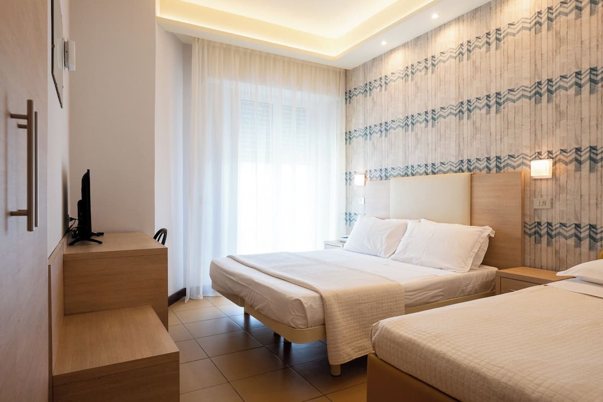 A hotel room with two beds, a desk, and a television.