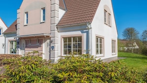 Une maison à deux étages, avec un toit recouvert de tuiles brunes, des murs extérieurs blancs et un numéro de maison bien visible.