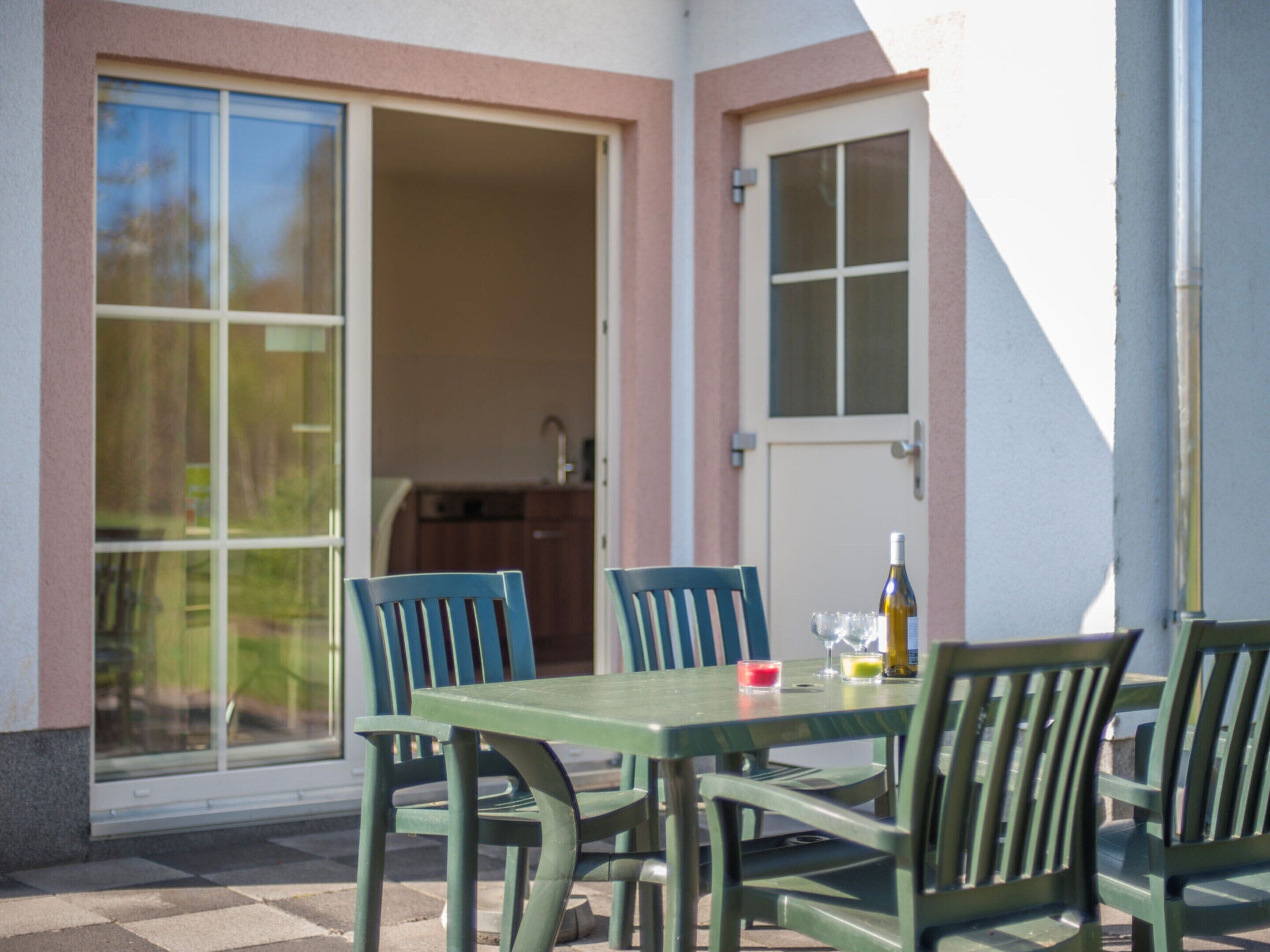An outdoor patio with a table and chairs, a bottle of wine, and a glass of red wine.