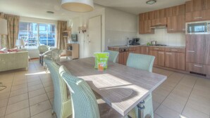 Une cuisine moderne avec des meubles en bois, un four à micro-ondes encastré et un coin repas agrémenté de chaises en osier et d’une table en bois.