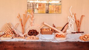 A table with various food items and breadsticks, with an abstract painting on the wall behind. - Sea Horse Hotel and Spa (Negombo)