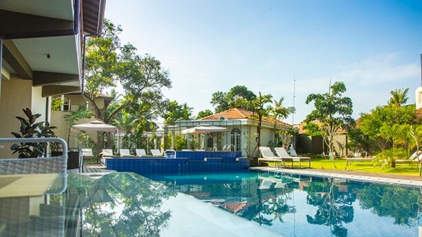 A swimming pool with lounge chairs and umbrellas, surrounded by greenery and a building with a tiled roof. - Sea Horse Hotel and Spa (Negombo)