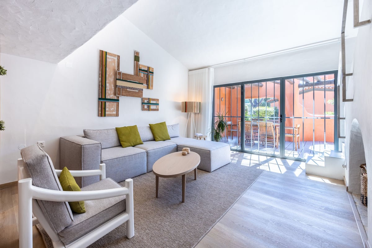 Un salon moderne avec un canapé gris, un fauteuil blanc et une table basse. Des œuvres d’art abstraites sont accrochées au mur au-dessus du canapé.