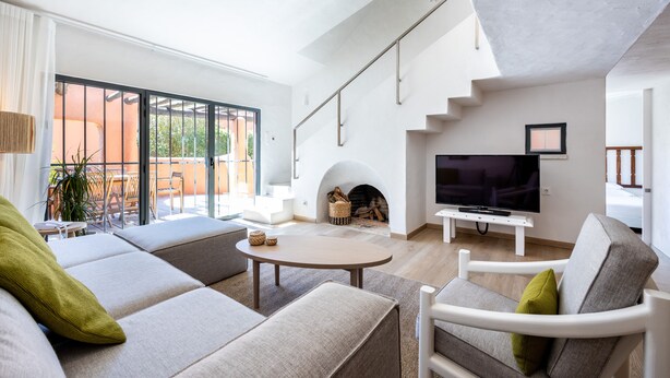 Una sala de estar moderna con un sofá, un sillón y una mesa de centro redonda. Hay una chimenea, un televisor y una escalera que lleva a otro nivel.