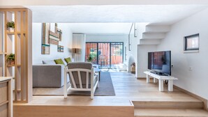 Una sala de estar moderna con sofá, sillón y mueble para televisión. Una escalera conduce a un espacio exterior.