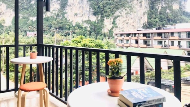 Un balcon agrémenté d’une table, de chaises et de plantes en pot, offrant une vue sur un paysage montagneux et un bâtiment.