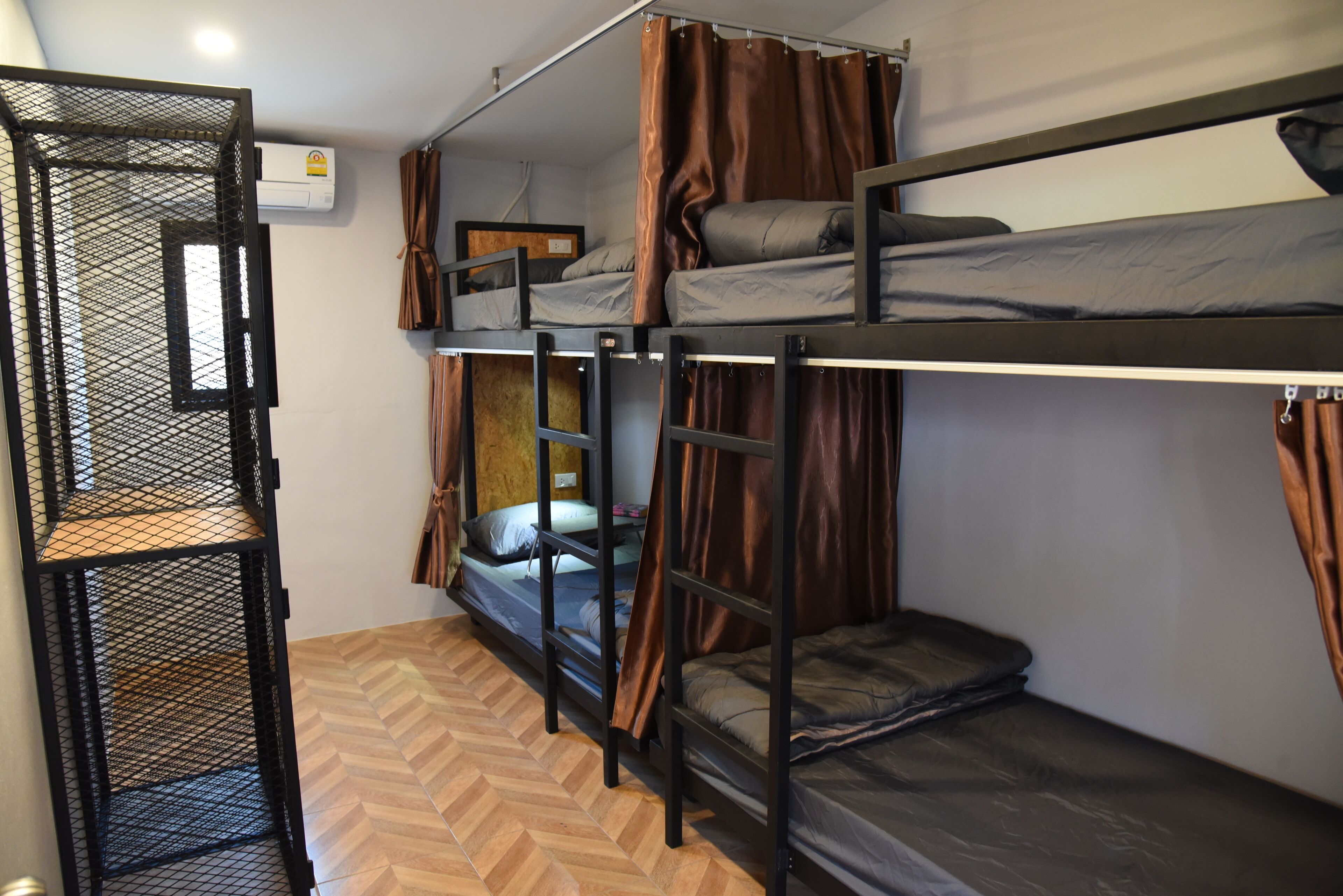 A bunk bed room with a metal ladder, a herringbone-patterned floor, and a window with curtains.