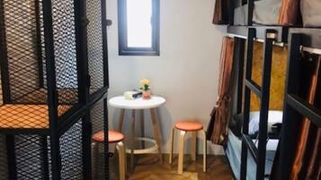 Una habitación pequeña con literas, una mesita redonda con taburetes y un equipo de aire acondicionado en la pared.