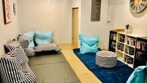 Un salon chaleureux avec un canapé d’angle, des coussins à rayures, un tapis bleu, une bibliothèque et une horloge murale.