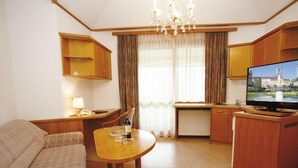 A compact hotel room with a sofa, a dining table, a television, and a kitchenette.