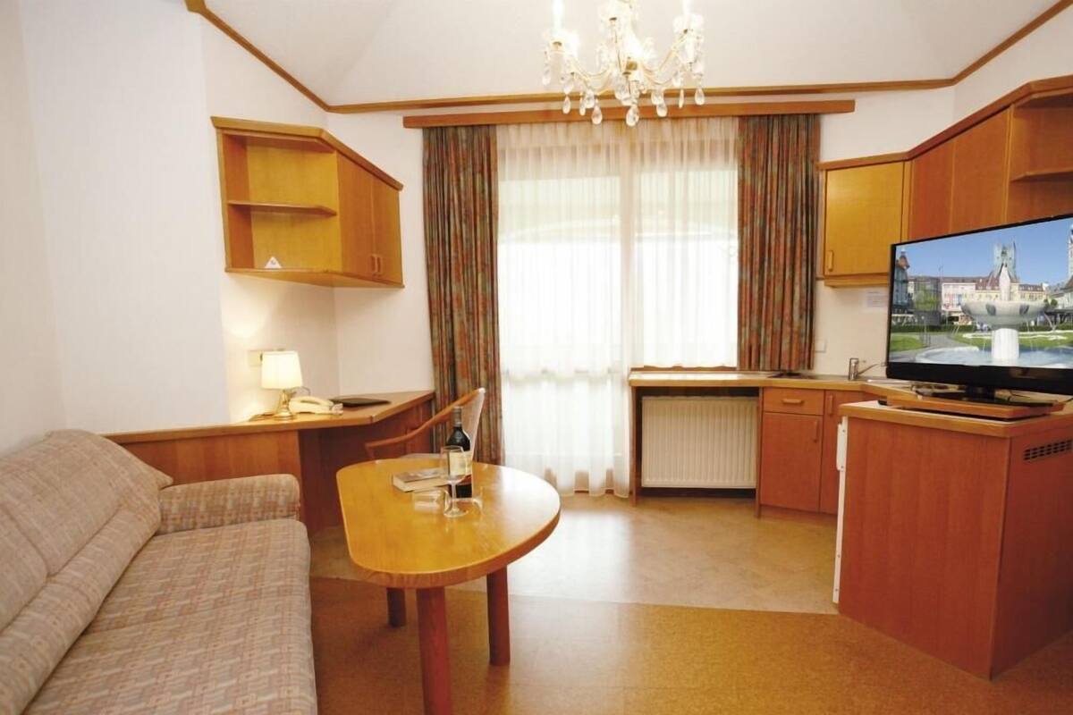 Une chambre d’hôtel compacte comprenant un canapé, une table à manger, un téléviseur et une kitchenette.