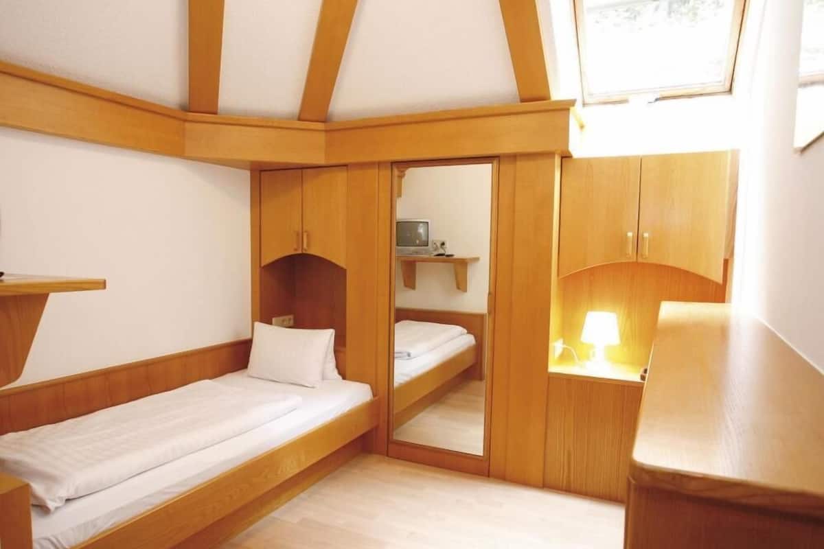 Une chambre de taille modeste, équipée de deux lits, d’un bureau et d’un miroir.