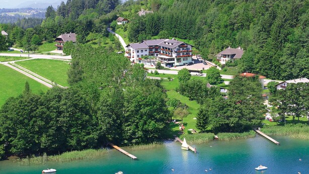 A large, multi-story building with a modern architectural style, surrounded by lush greenery and a lake with boats.