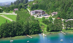 Un edifici gran de diversos pisos amb un estil arquitectònic modern, envoltat de vegetació abundant i un llac amb barques.