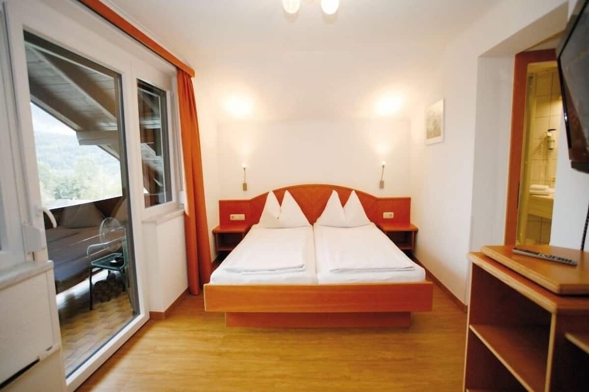 Une chambre avec un grand lit, une tête de lit en bois, deux tables de chevet, un miroir et une porte-fenêtre coulissante donnant sur un balcon.
