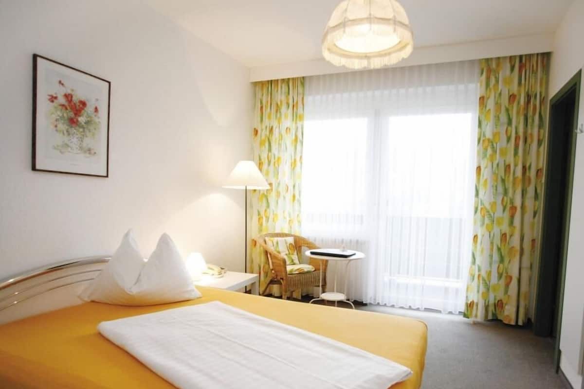 Une chambre d’hôtel avec un lit, une chaise, une petite table et une lampe.
