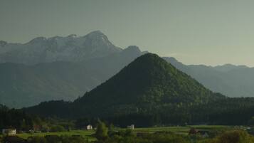 A mountainous landscape with a prominent hill in the foreground and a range of mountains in the background. There are buildings and greenery in the valley below.