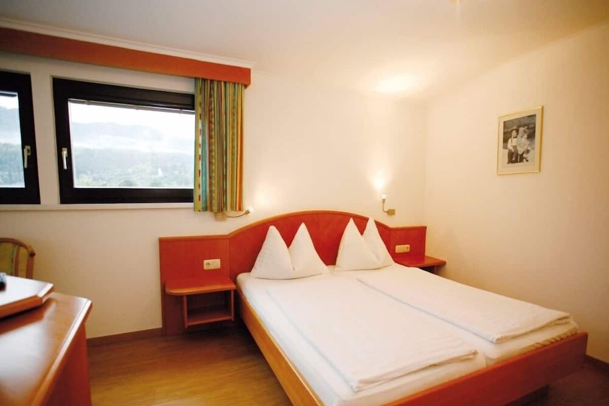 Une chambre d’hôtel avec un grand lit, un bureau, une chaise, une fenêtre avec des rideaux et un tableau encadré au mur.