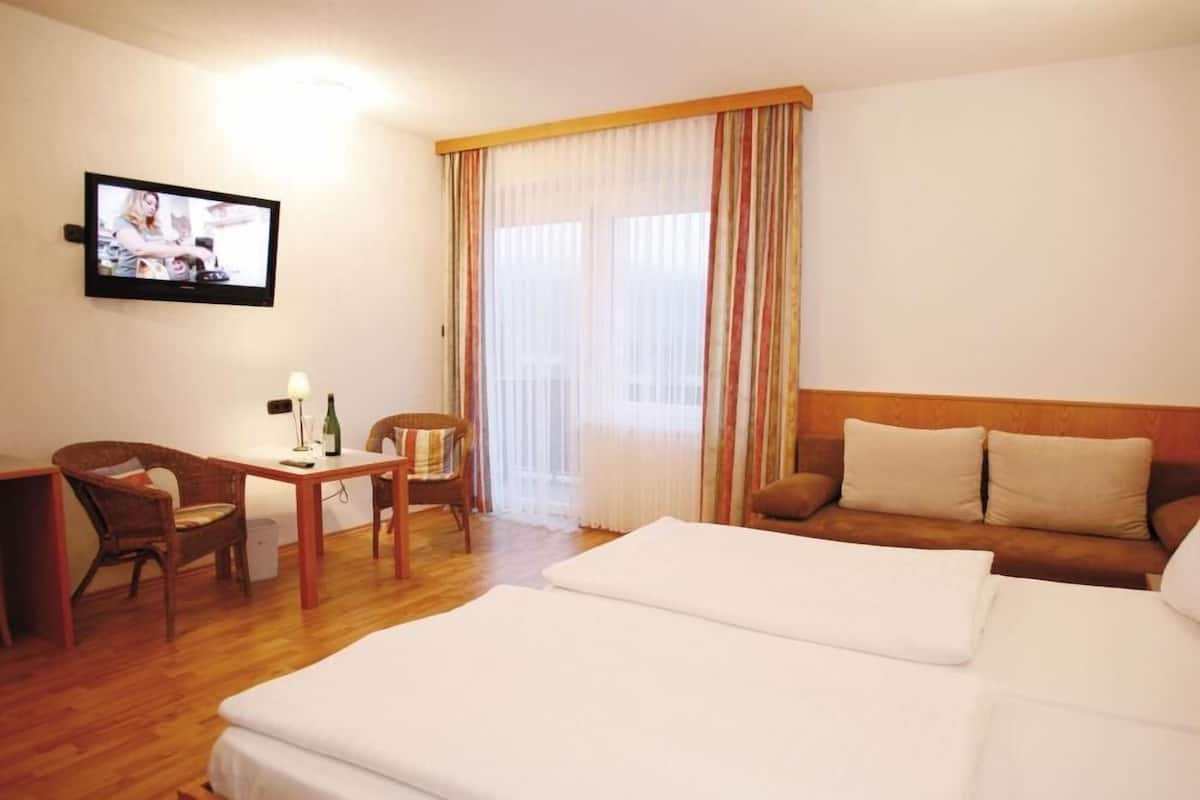 Une chambre d’hôtel comprenant un lit, un canapé, un bureau avec une chaise, une télévision et une fenêtre avec des rideaux.