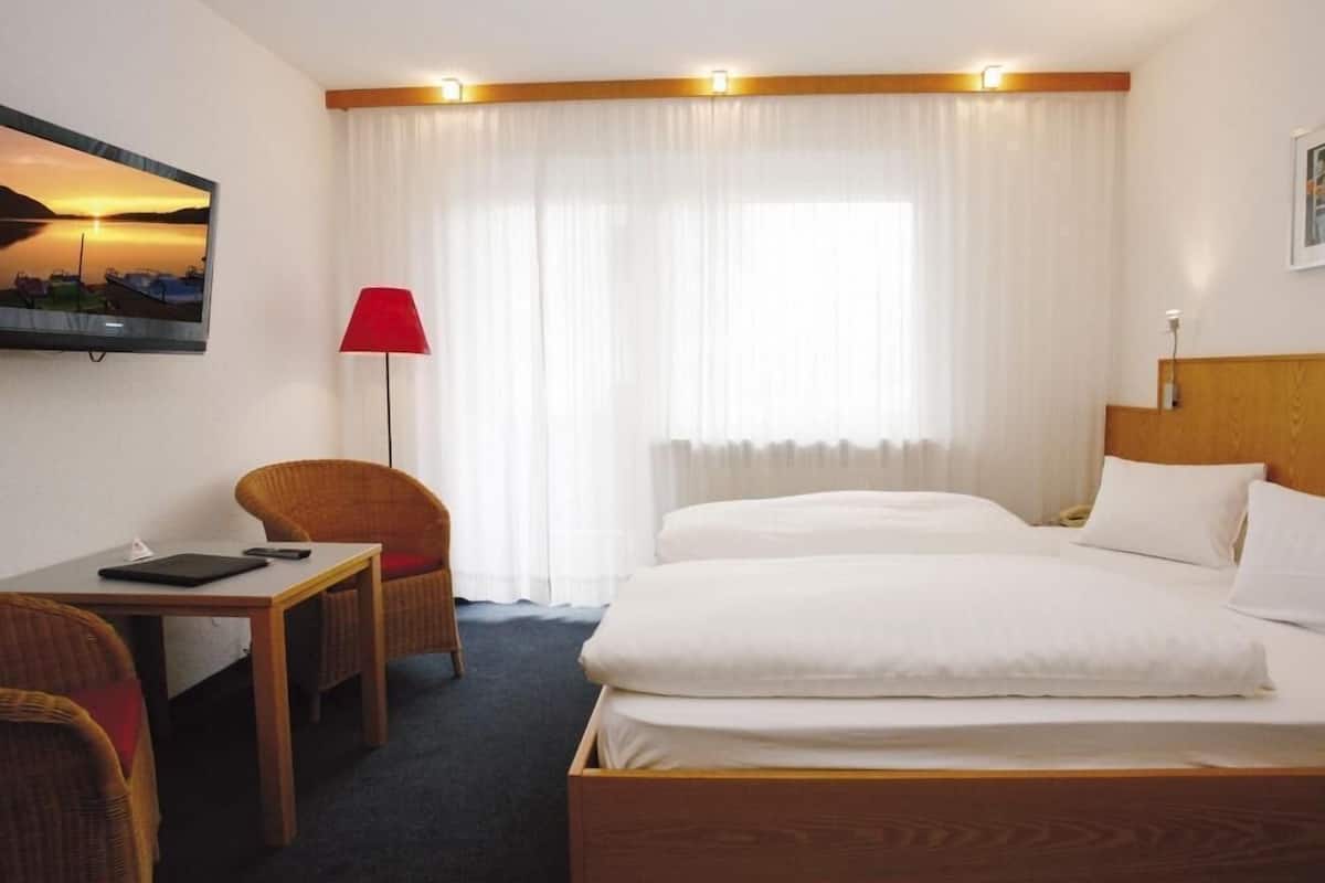 Une chambre d’hôtel avec un lit, un bureau, une chaise, une lampe rouge et un tableau au mur.