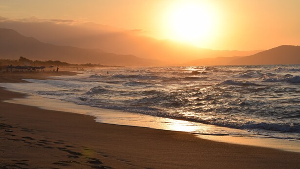 Ein Strand mit Wellen und einem Sonnenuntergang.