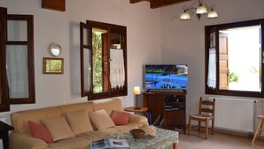 Ein gemütliches Wohnzimmer mit einer Couch, einem Fernseher und einem Fenster mit Vorhängen.