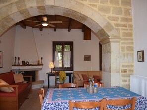 A cozy living room with a stone archway, a fireplace, a dining table with chairs, and a sofa.
