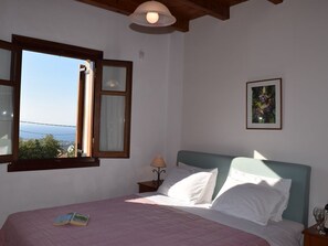 A bedroom with a bed, a window, a nightstand, a lamp, and a framed picture on the wall.