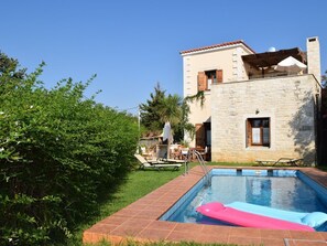 A swimming pool with a pink float, a stone building with a balcony, and a well-maintained garden.