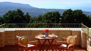 Eine Terrasse mit Tisch und Stühlen, einer Blumenvase und Blick auf die Berge.
