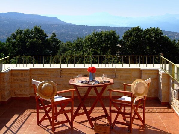 Una terraza con una mesa y sillas, un florero con flores y vistas a montañas.
