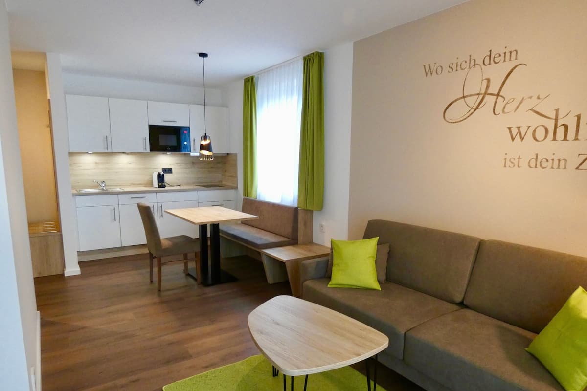 A compact living space with a kitchenette, a dining area, and a sofa with green cushions.