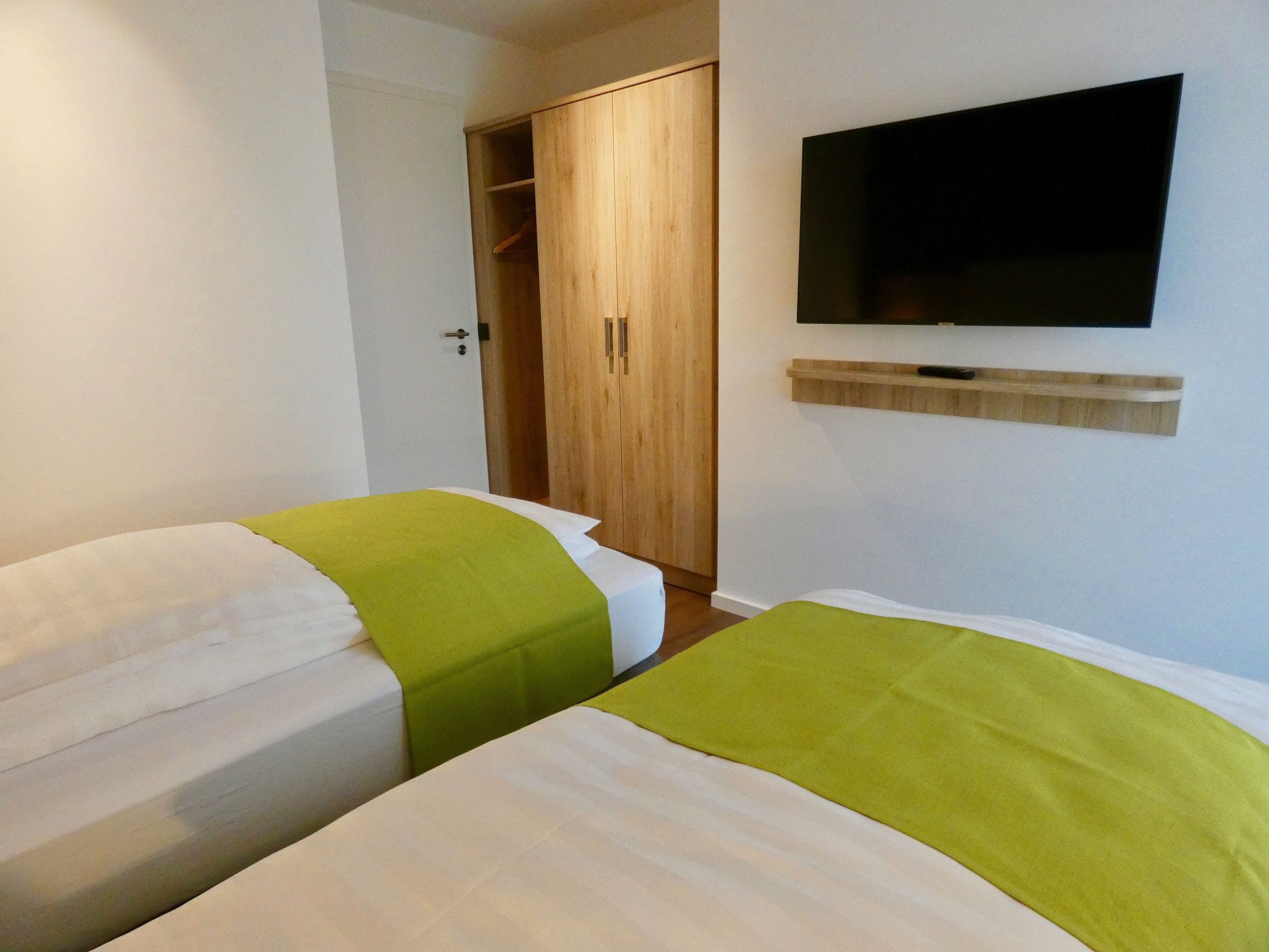 Habitació d'hotel amb dos llits, un armari de fusta, un televisor penjat a la paret i una estant a sota.