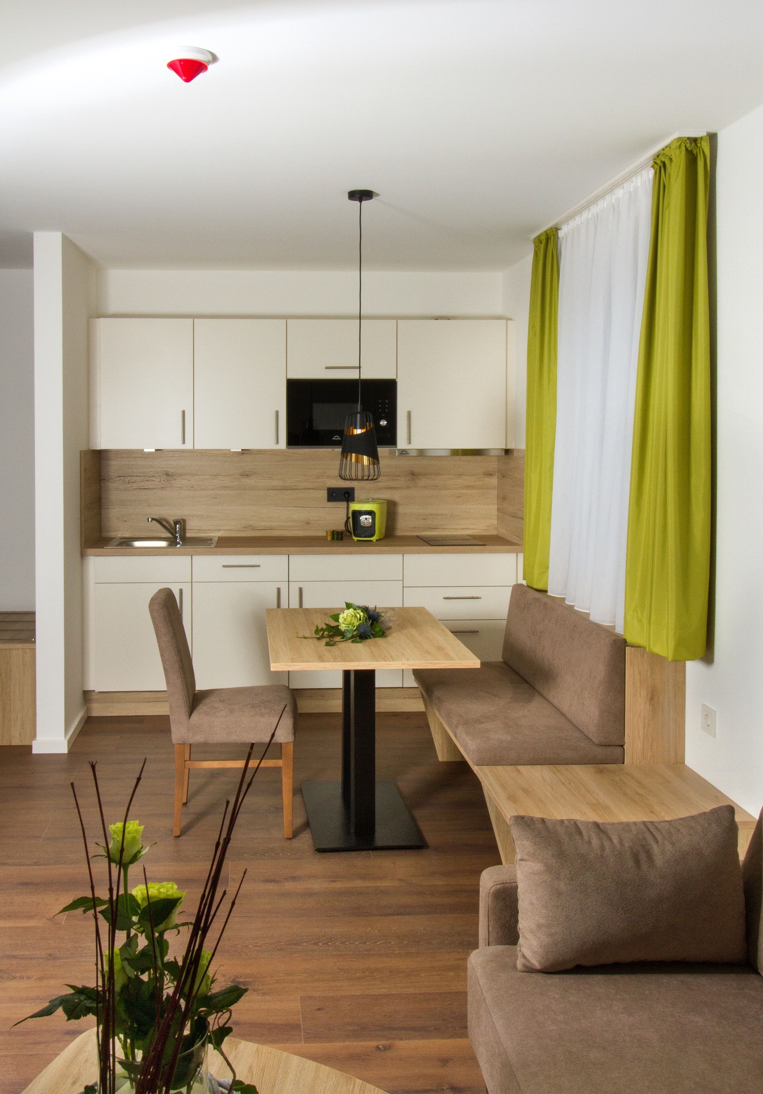 Eine moderne Küche mit weißen Schränken, einer schwarzen Mikrowelle und einer Holzausziehtafel. Es gibt einen Esstisch mit Stühlen und einer Bank.