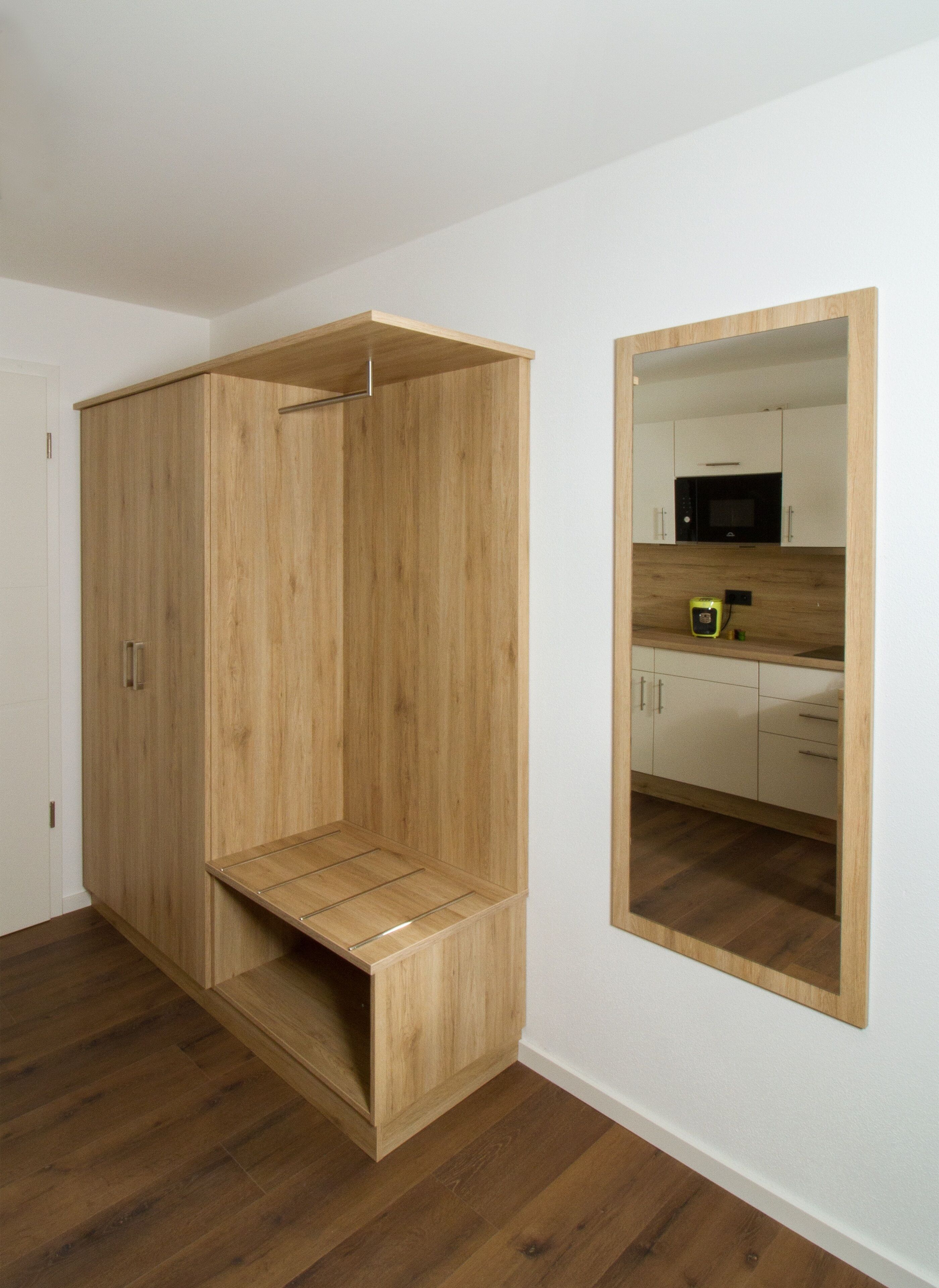 Una habitación con un armario de madera, un espejo y una zona de cocina con armarios y un microondas.