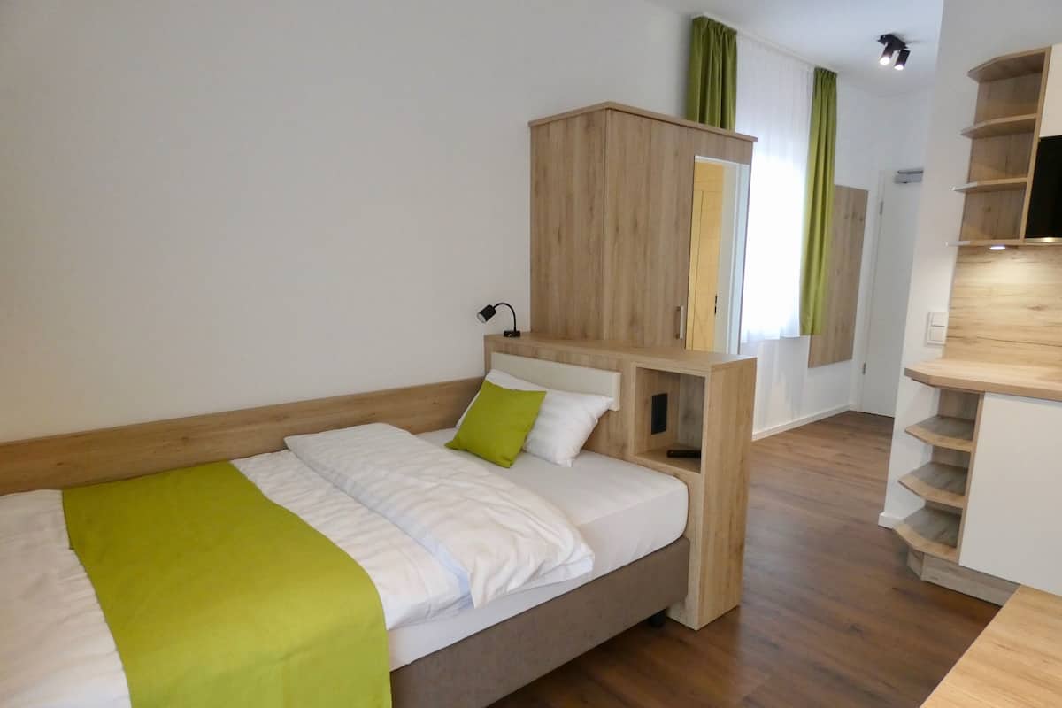 A modern bedroom with a wooden bed frame, a green throw blanket, and built-in wooden shelving.