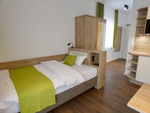 Une chambre moderne avec un cadre de lit en bois, un plaid vert et des étagères intégrées en bois.
