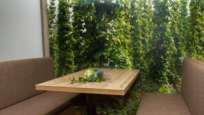 Ein kleiner Holztisch mit floraler Dekoration, umgeben von braunen Sitzgelegenheiten vor einem Hintergrund aus dichtem Grün.