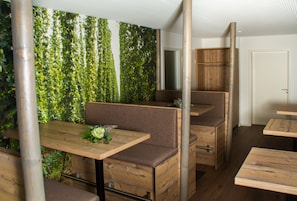 A restaurant with wooden furniture and a green leafy wall.