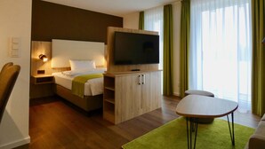 Ein Hotelzimmer mit einem Bett, einem an einer Holzkommode befestigten Fernseher, einem kleinen Tisch und einem grünen Teppich.