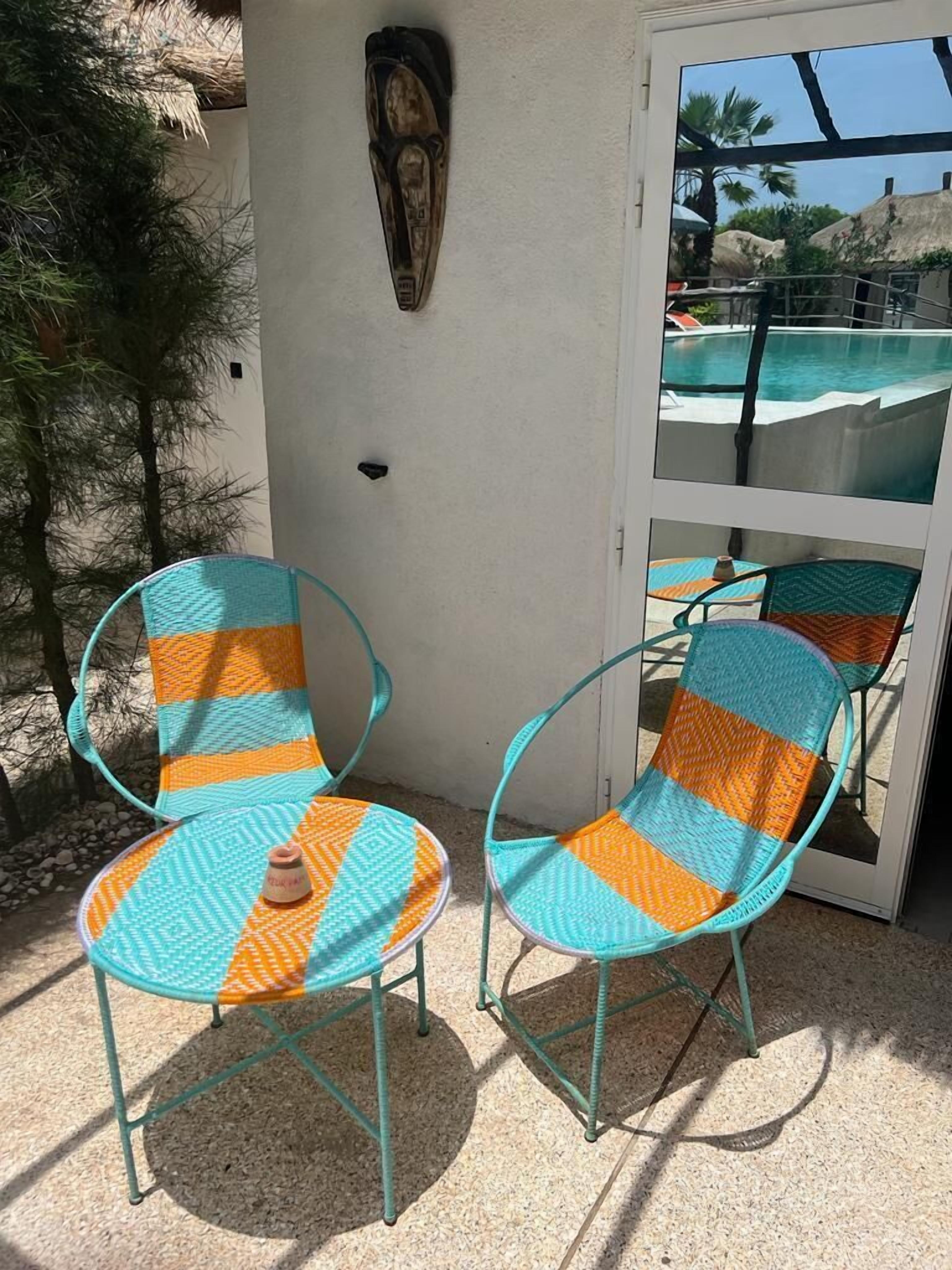 Two turquoise and orange striped lounge chairs with a small table, a decorative wall piece, and a glass door leading to a pool area.