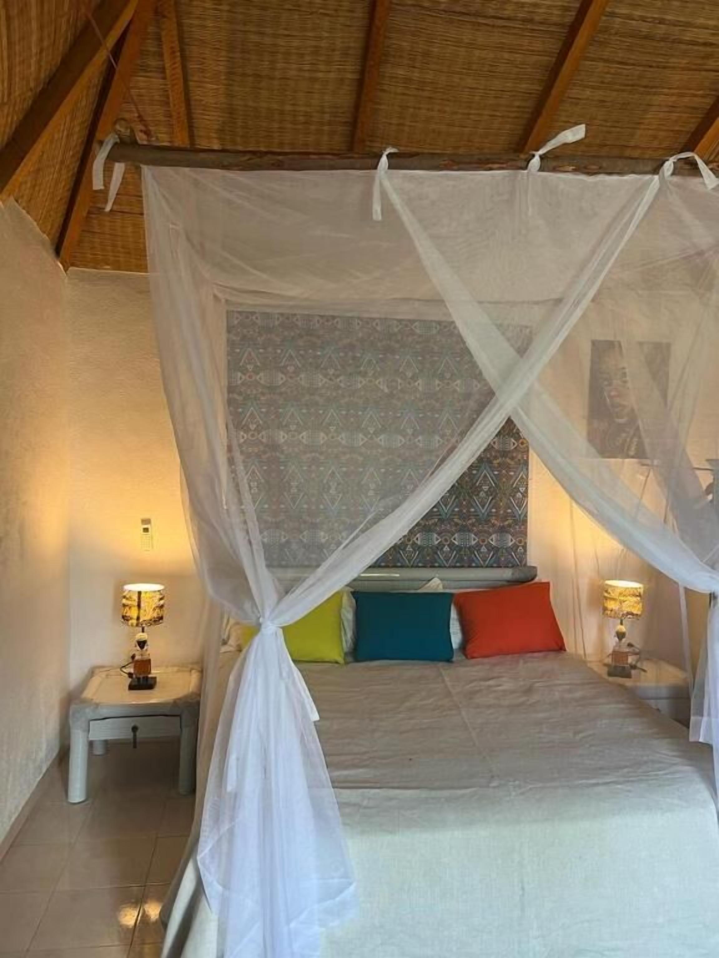 A bedroom with a canopy bed, two bedside tables with lamps, and patterned wall decor.