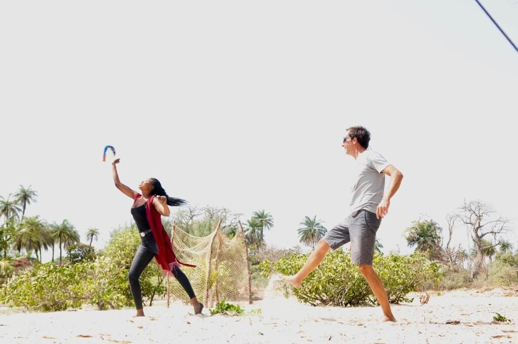 Two people playing a sport on a beach with palm trees and a clear sky.