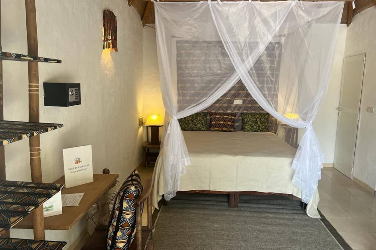 Une chambre avec un lit sous un dais, un bureau avec une chaise, une lampe et un panneau accroché au mur.