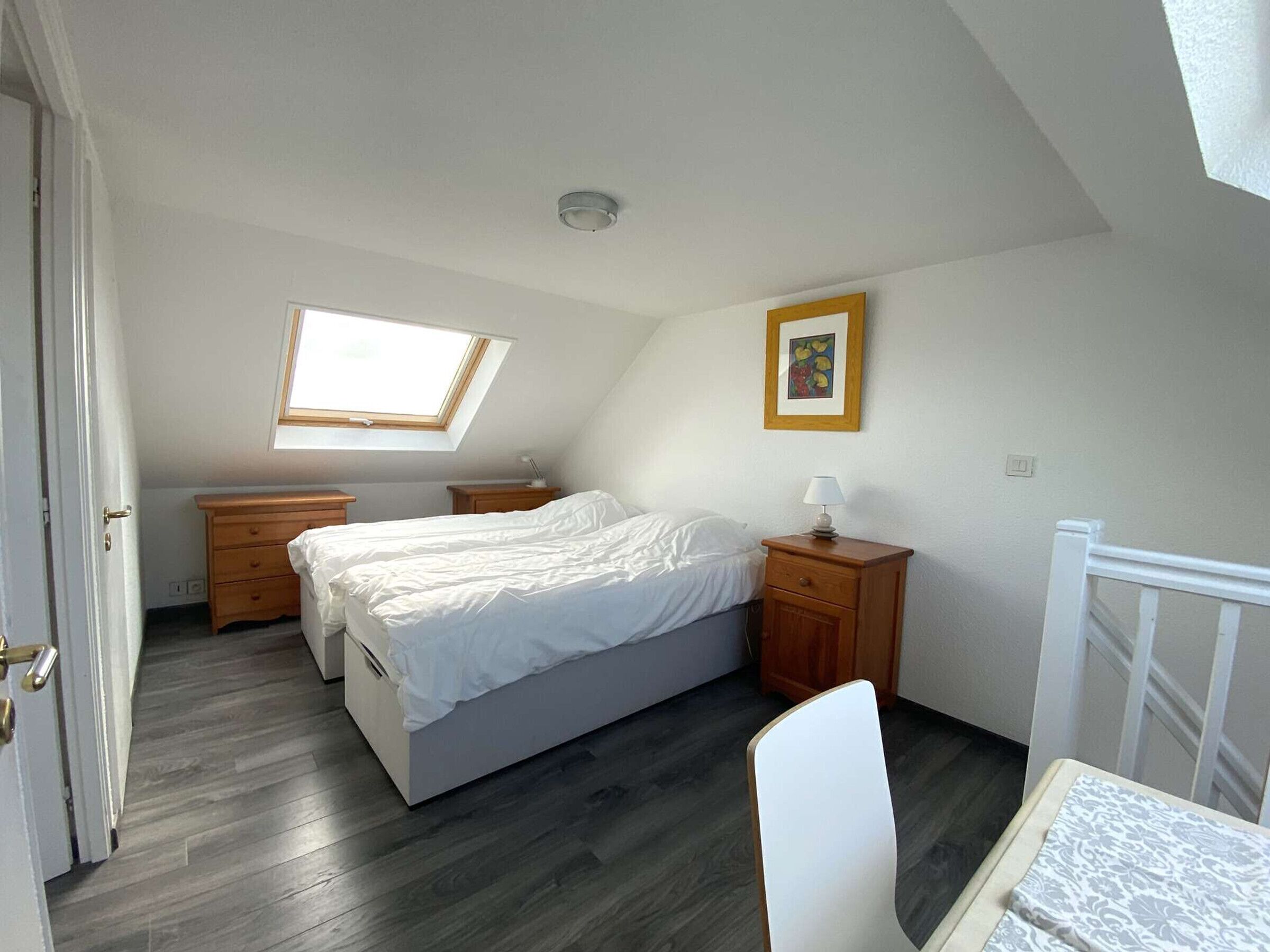 A bedroom with a bed, two nightstands, a desk, a chair, a window, and a picture on the wall.