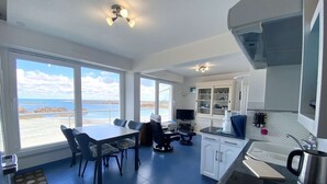 A modern kitchen with a dining area, large windows with a view of the sea, and a built-in oven.