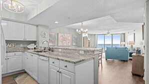A spacious kitchen with white cabinets, granite countertops, and a view to the living area.