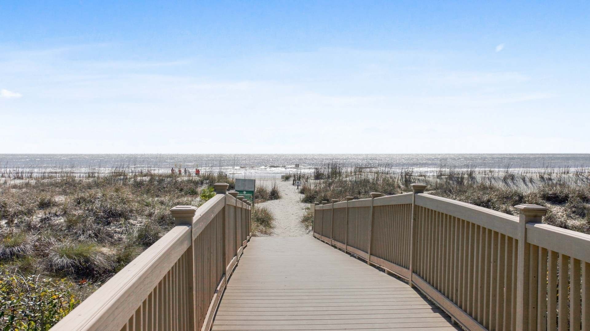 Une promenade en bois qui mène à une plage d’où l’on a une vue dégagée sur l’océan.