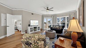 Un salon avec un canapé, un pouf et un téléviseur posé sur un meuble.